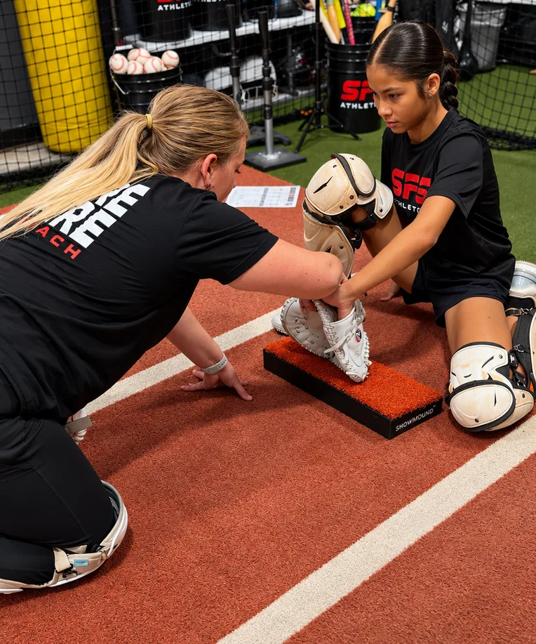 An SFS coach working with a young catcher on blocking technique