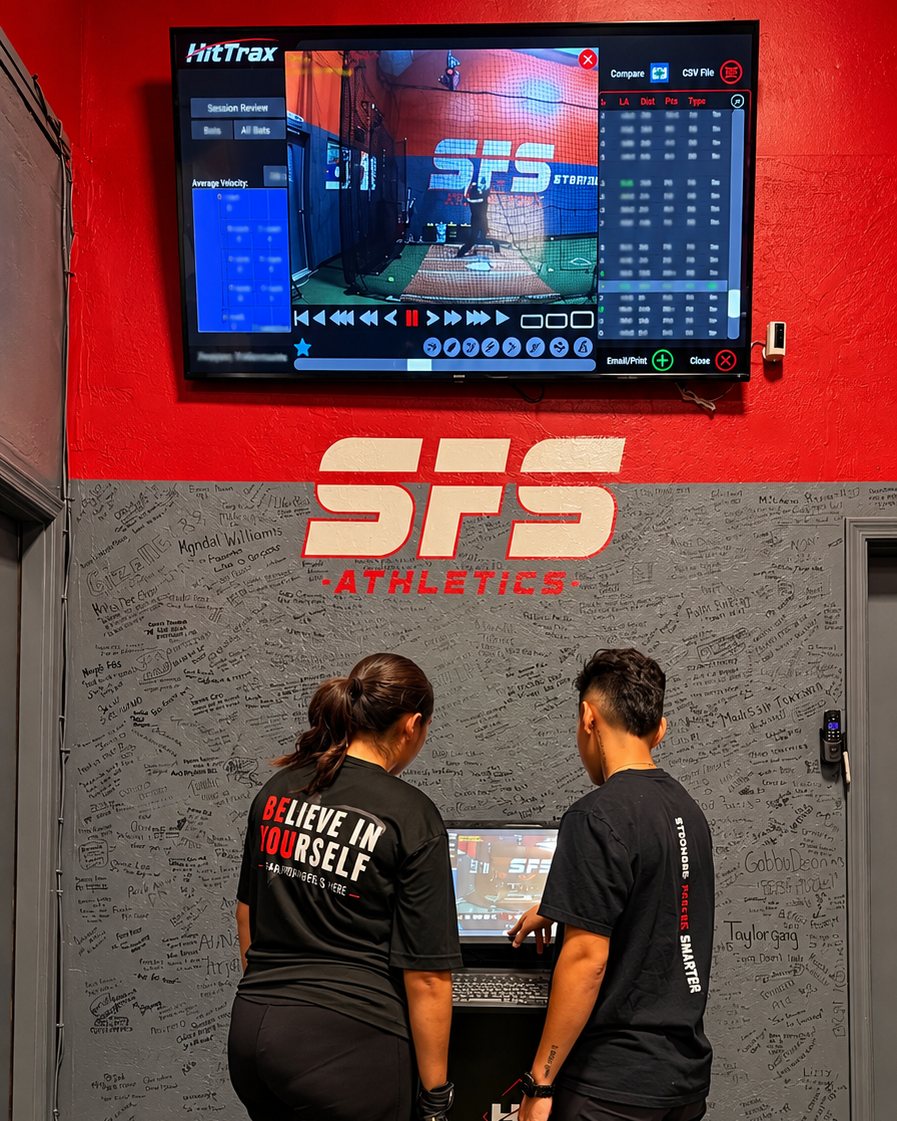 An SFS coach and athlete reviewing swing video and data on the HitTrax screen