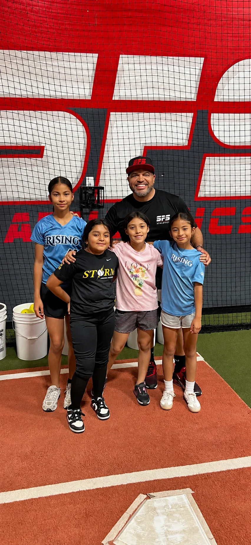 BJ Johnson with four young athletes in front of the SFS Athletics wall in the hitting tunnel